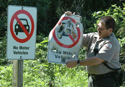 A ranger holding up a beat up sign, next to a new sign