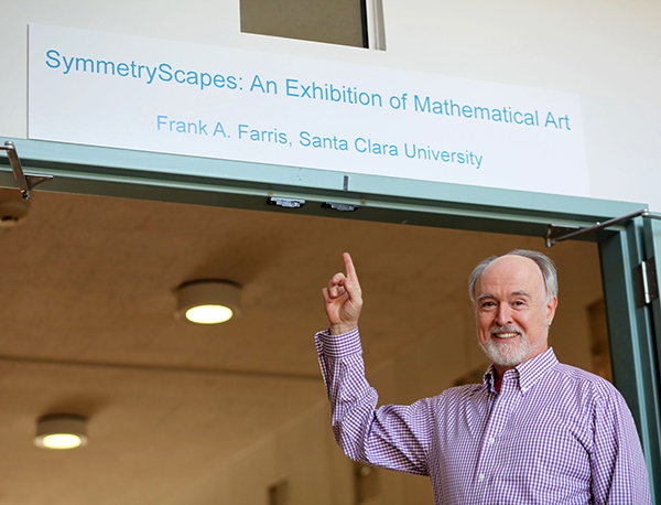 Farris before a sign that says SymmetryScapes: An Exhibition of Mathematical Art